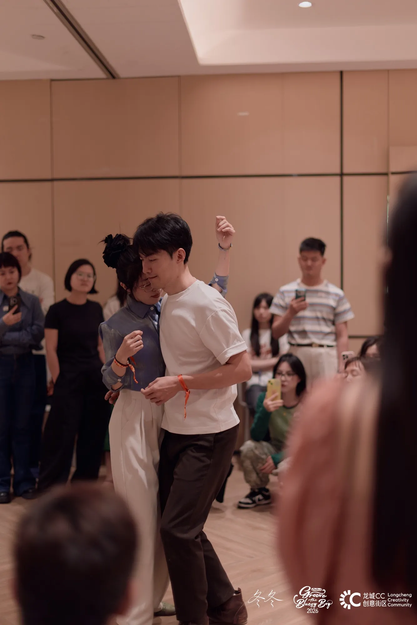 Lucas and Penny demonstrating a close-embrace blues move while students watch and film